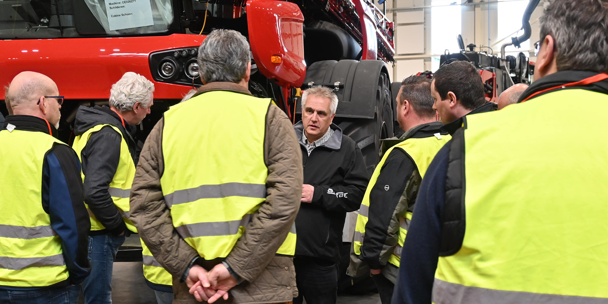 A group of people gathered around an Agrifac sprayer inside a spacious factory, discussing its features and functionality.