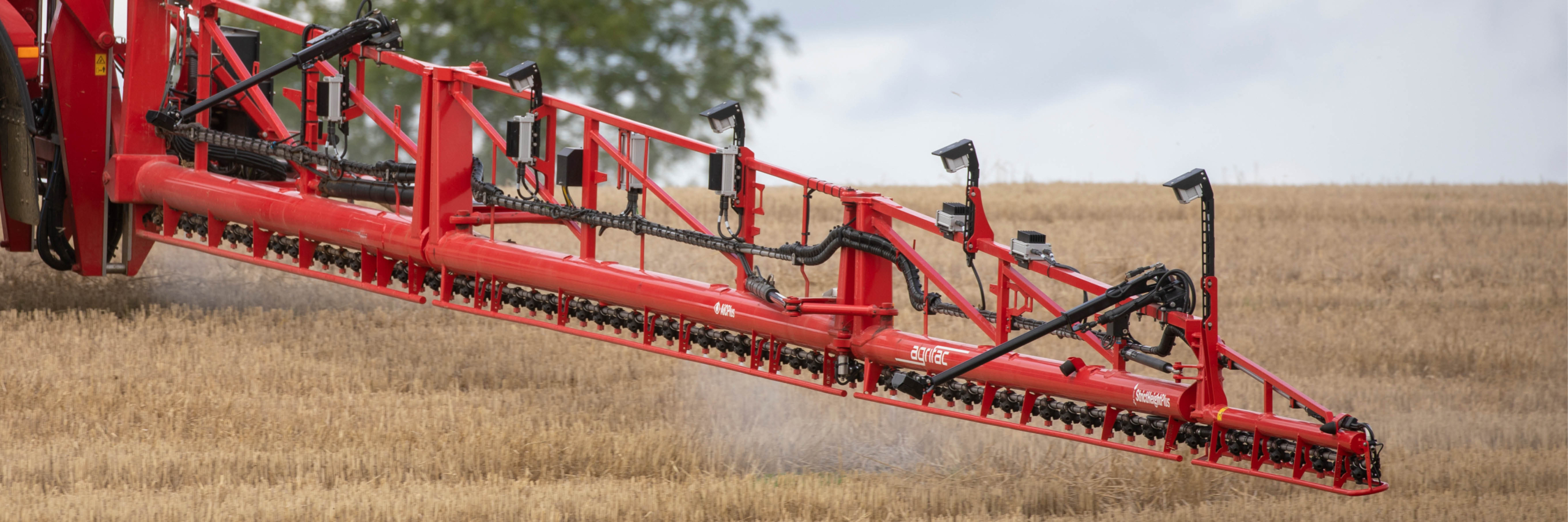 An Agrifac sprayer boom with camera spot spray system spraying efficiently in a vast field, under a clear blue sky.