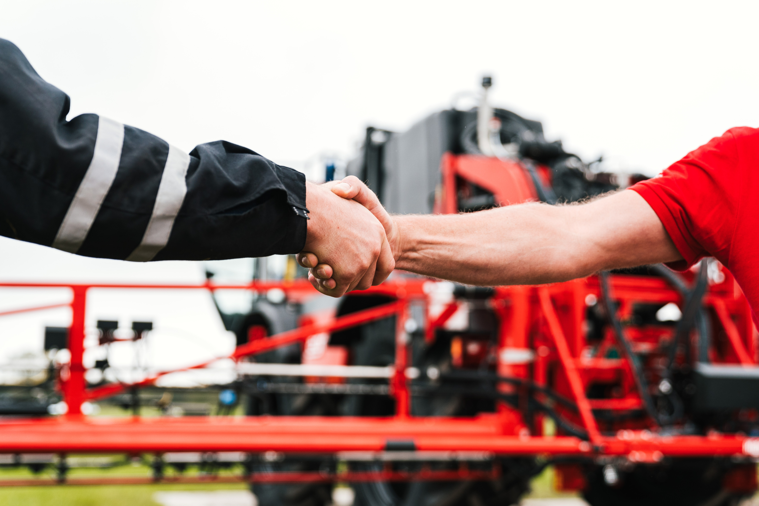 Two men shaking hands in front of an Agrifac machine.