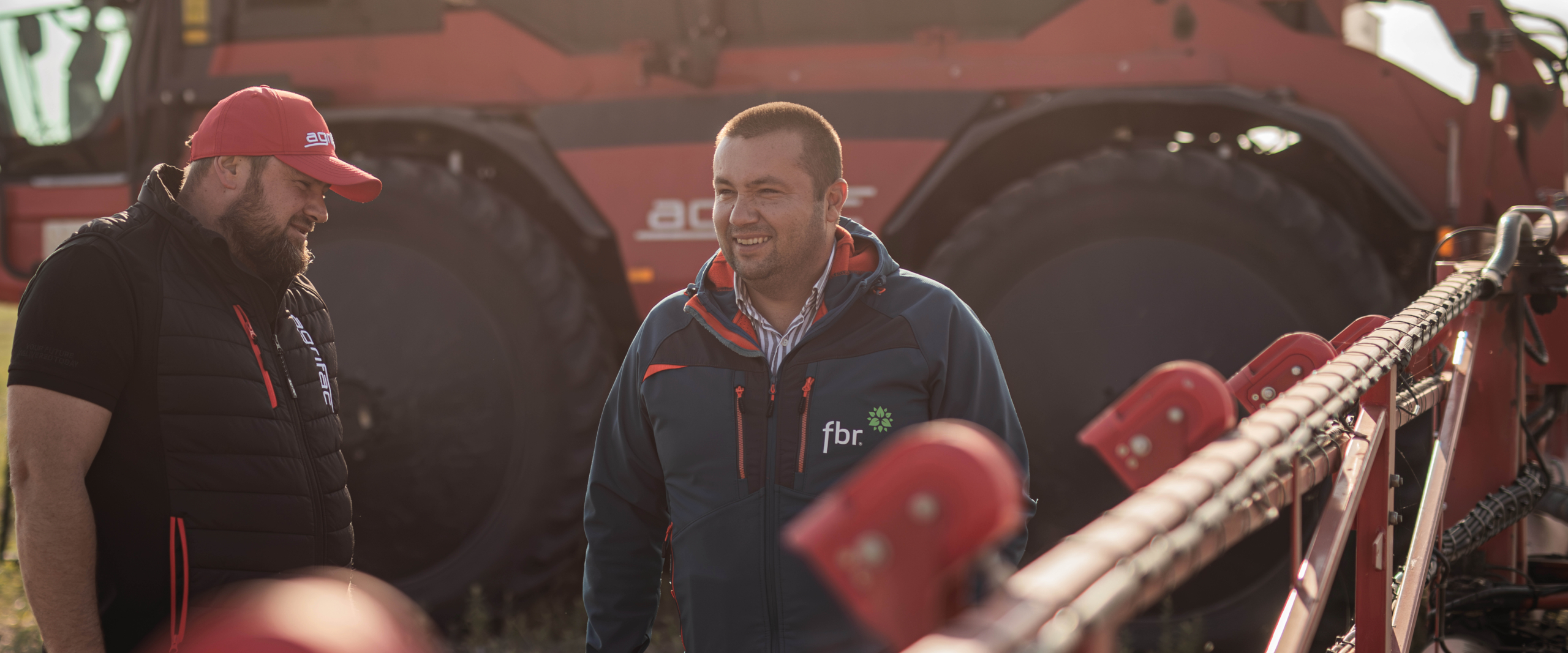 Two men smiling next to an Agrifac sprayer.