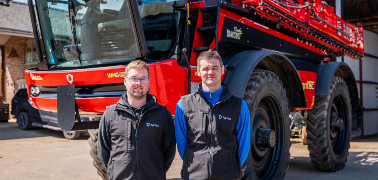 Two men stand beside an Agrifac sprayer, showcasing its size and machinery in an outdoor setting.