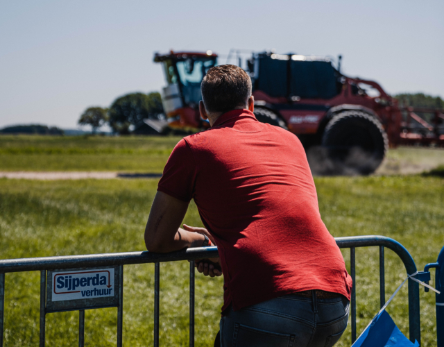 Person leaning over a fence watching a sprayer.