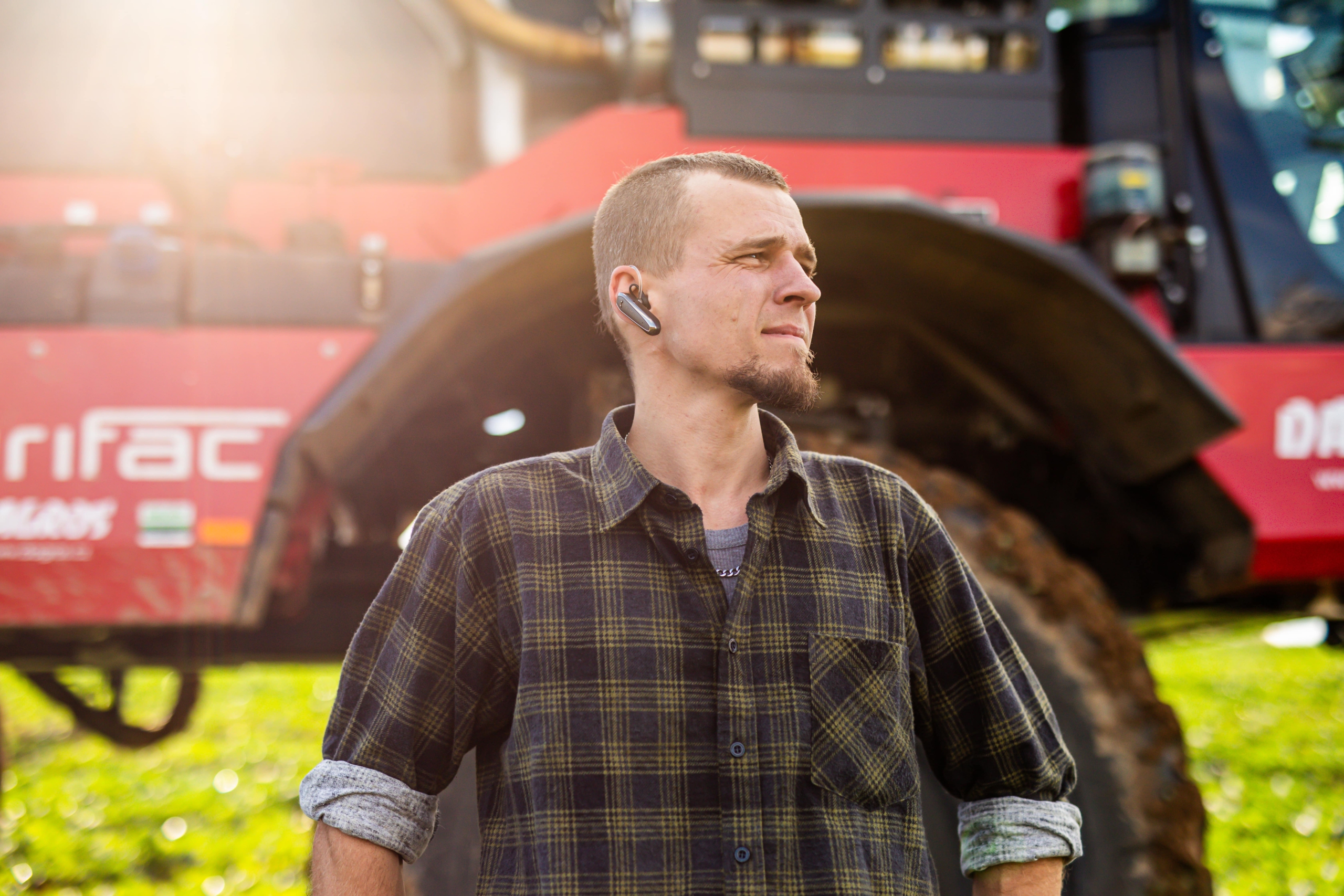 A man stands confidently in front of a large Agrifac sprayer, showcasing his connection to agricultural machinery.