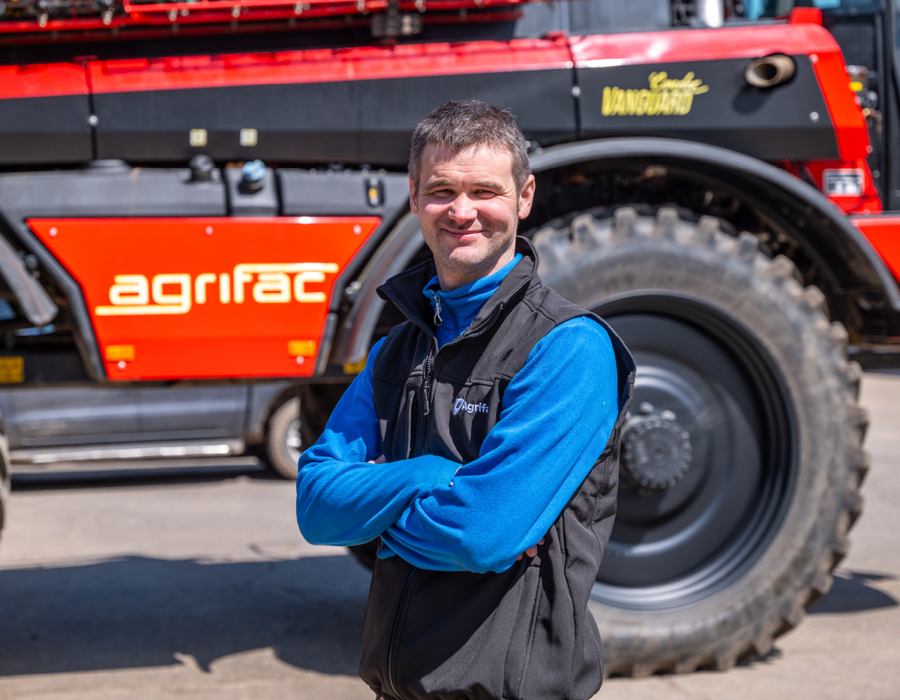 A man stands confidently in front of an Agrifac sprayer, showcasing its impressive size and machinery.